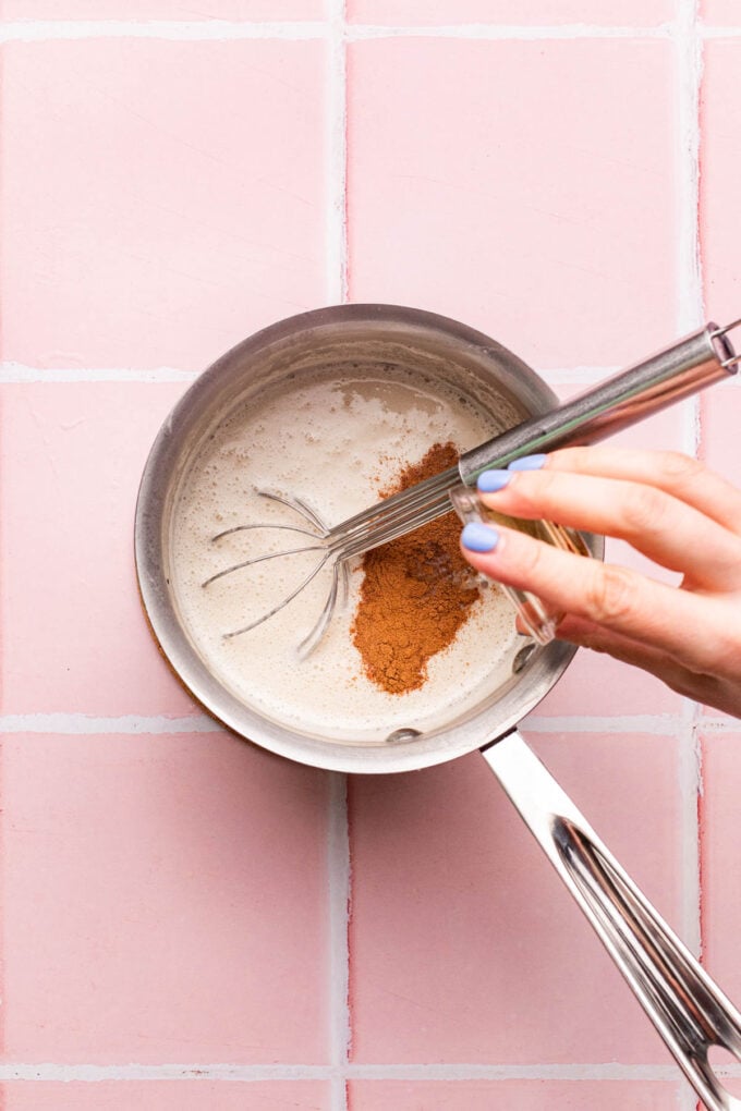 hand adding cinnamon to a pot of oats