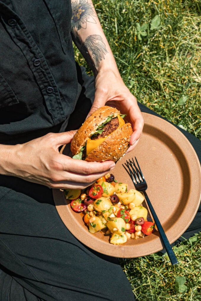 hands holding burger with plate of salad