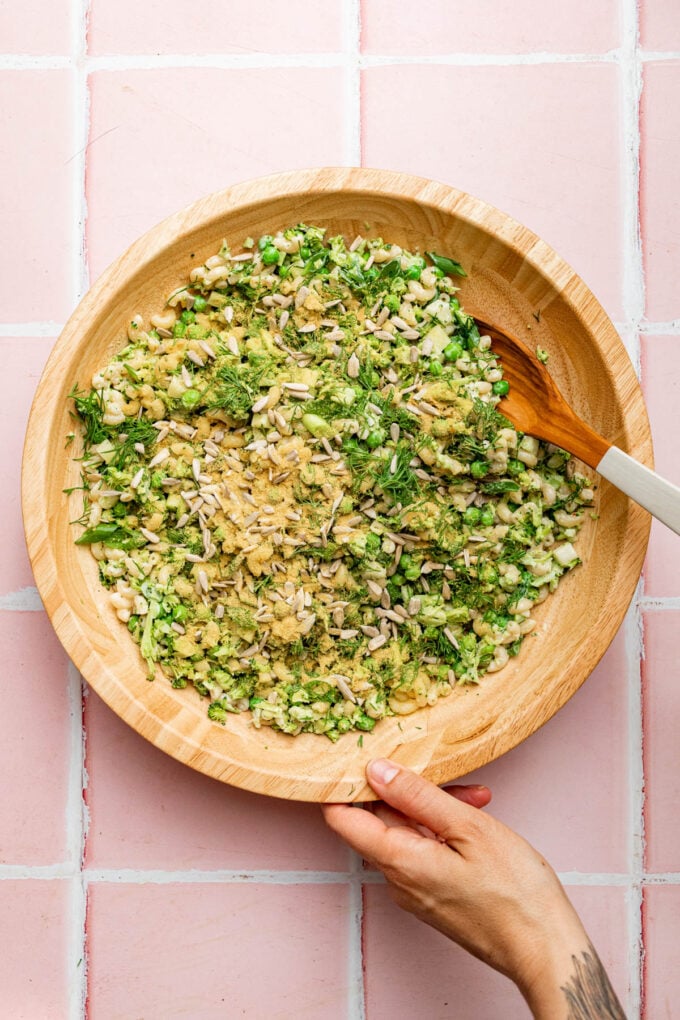 hand tossing pasta salad in wooden bowl