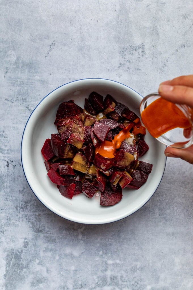 hand pouring dressing on beets