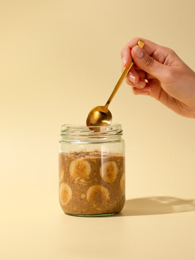 hand with gold spoon and banana oats in jar