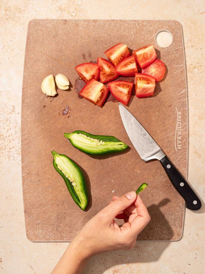 hand holding jalapeño slice with cutting board and knife