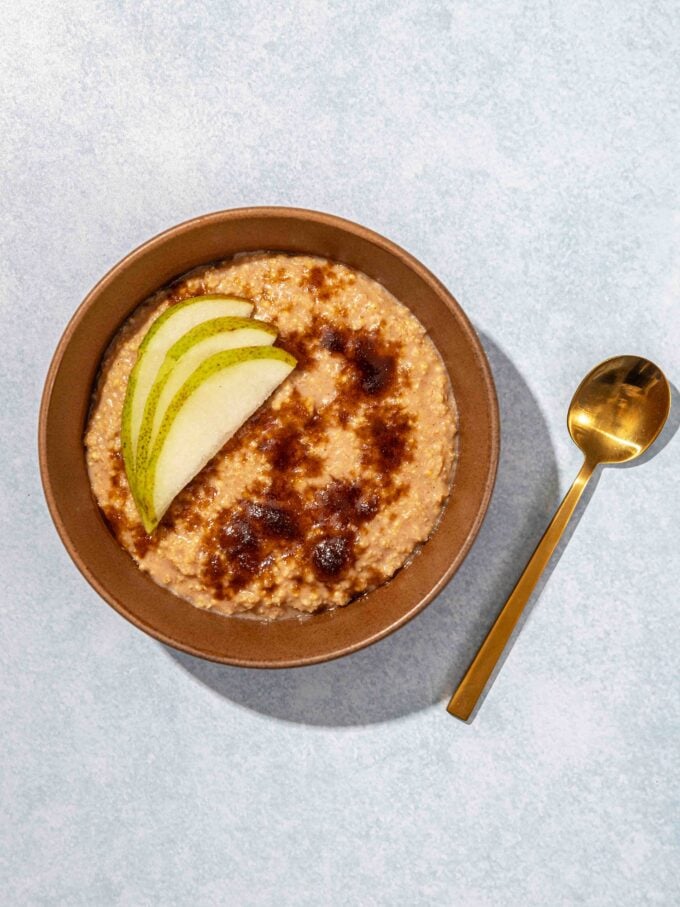 millet porridge in brown bowl with sugar and sliced pear