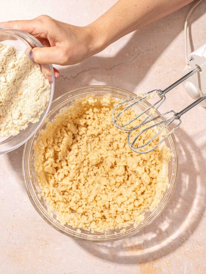 hand pouring flour into bowl of butter