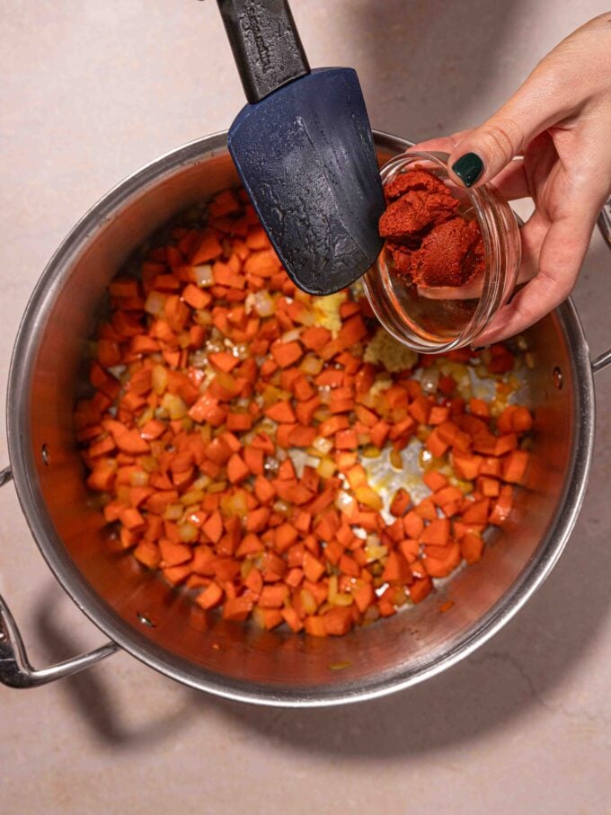 hand adding curry paste to vegetables in pot