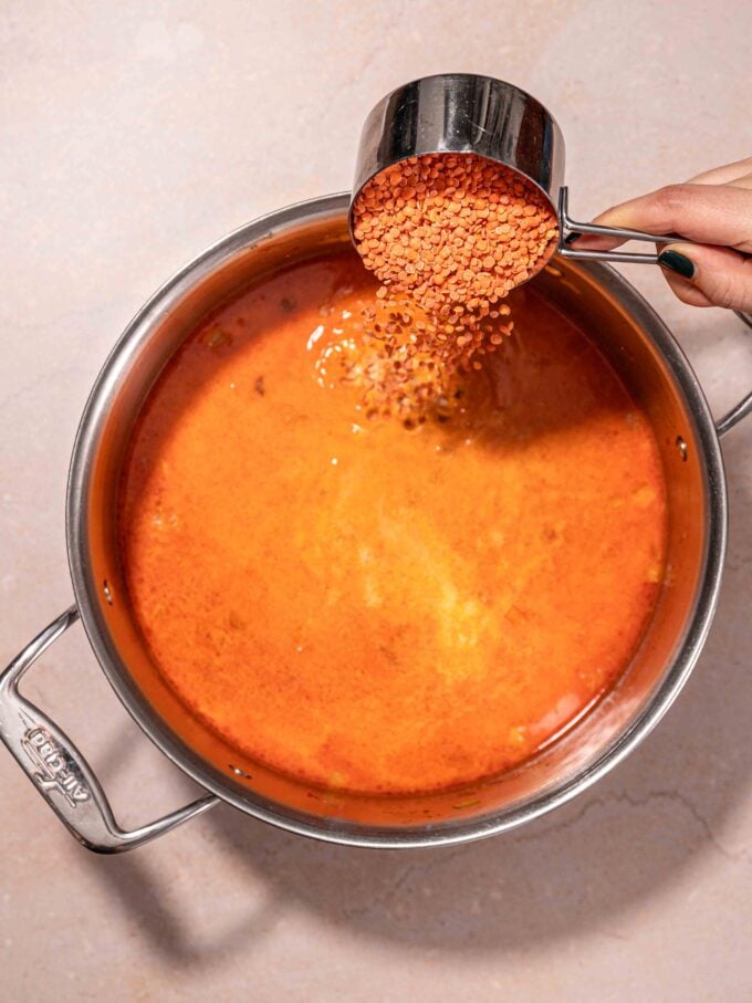 hand adding lentils to soup pot