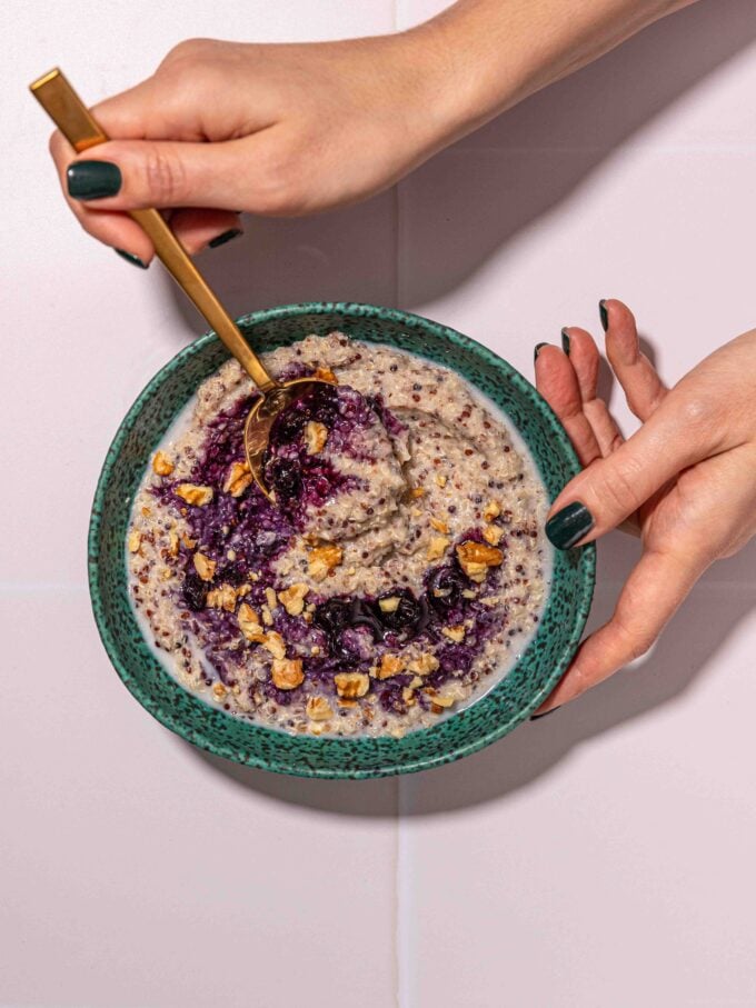 hand holding blue bowl of quinoa porridge with blueberries