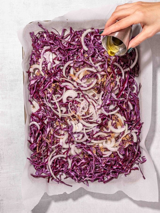 hand pouring oil over tray of red cabbage and red onion