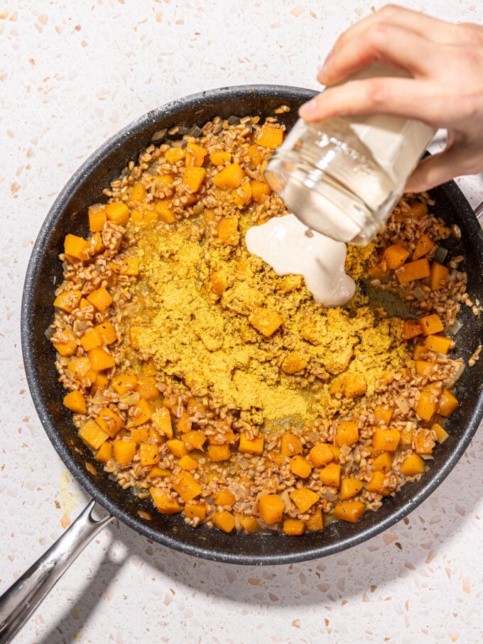 hand pouring cashew cream into vegan farro risotto