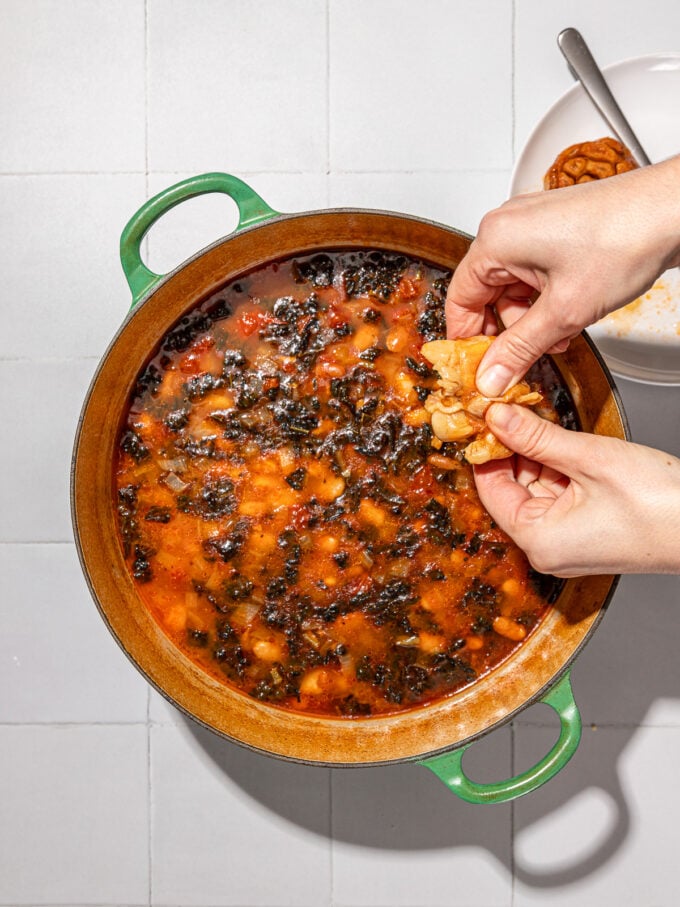 hand squeezing garlic into pot of beans