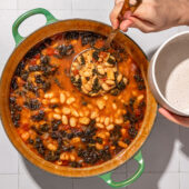 hand ladling brothy beans into bowl