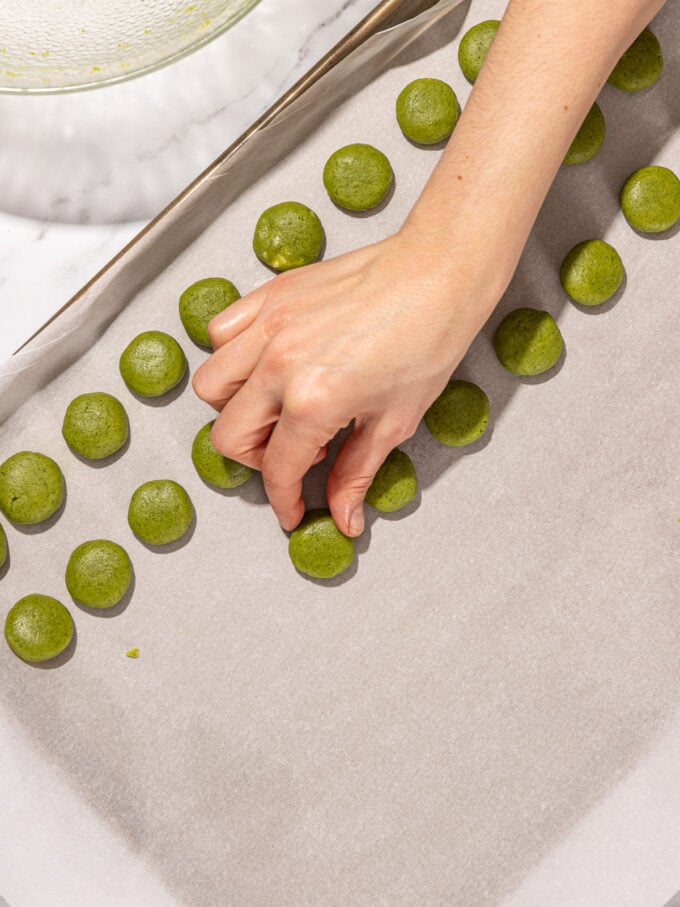 hand placing matcha cookie on baking sheet