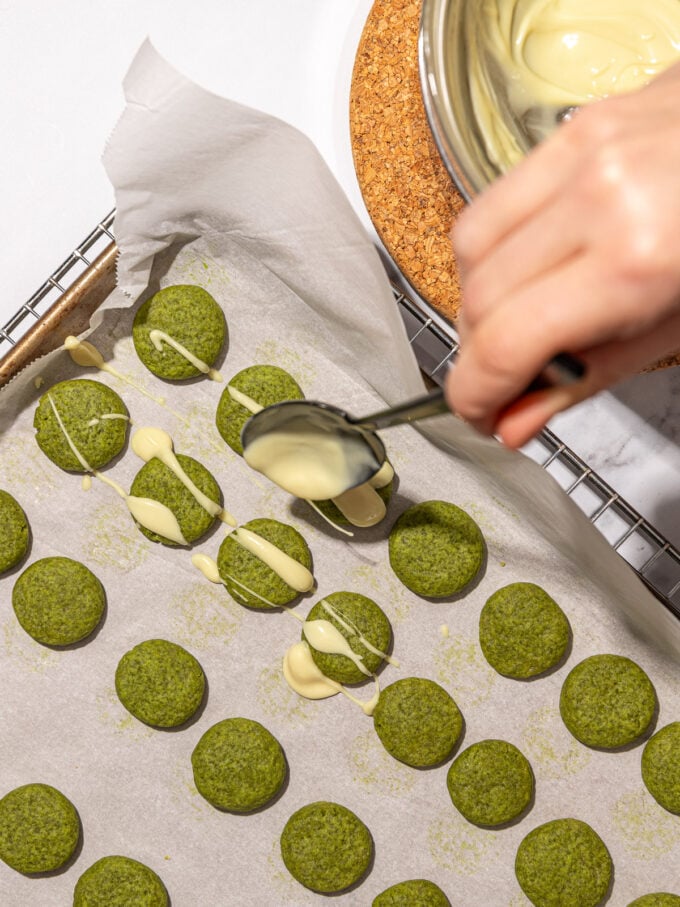 hand drizzling white chocolate over matcha cookies