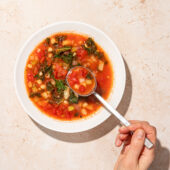 hand with spoon in bowl of vegetarian navy bean soup