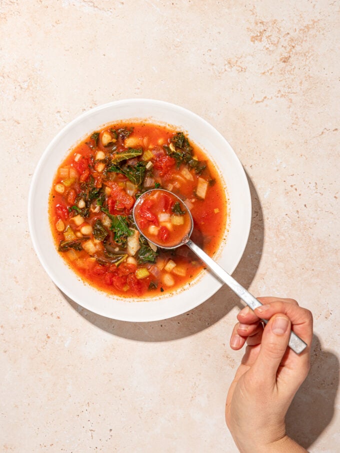 hand with spoon in bowl of vegetarian navy bean soup