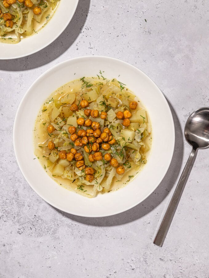 bowls of green cabbage soup with potato and chickpeas and spoon