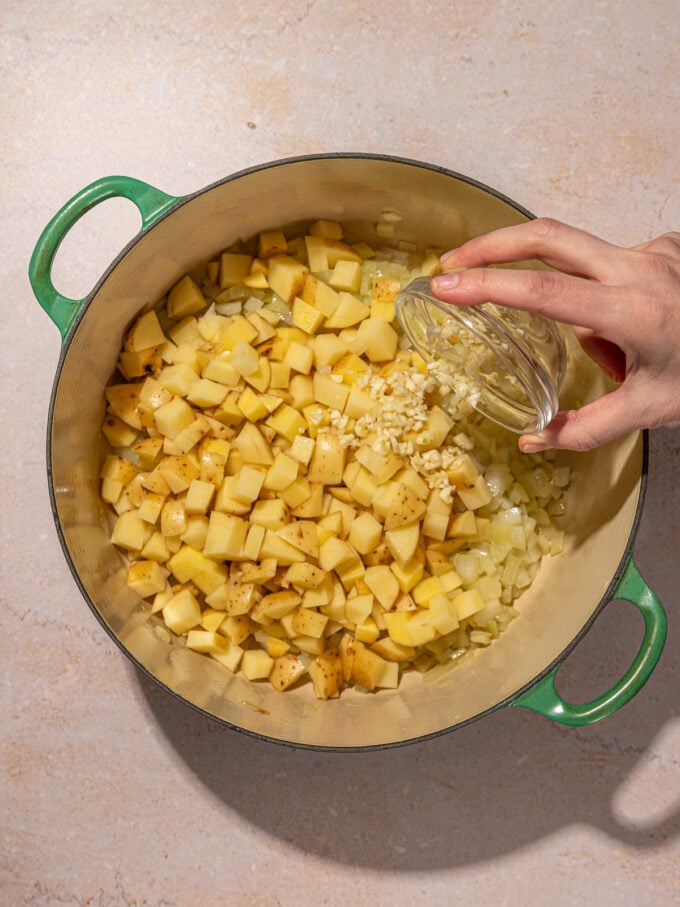 hand pouring garlic into pot of potatoes