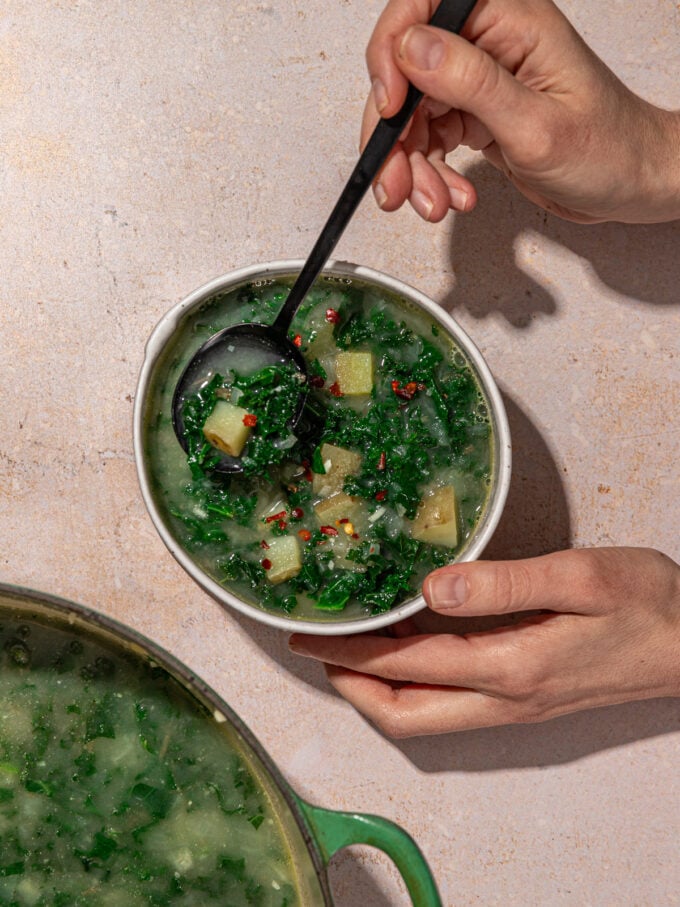 hands holding bowl of kale and potato soup