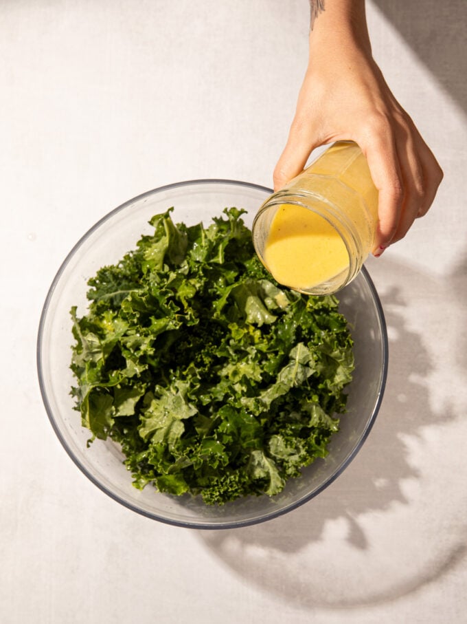 hand pouring lemon dressing onto kale