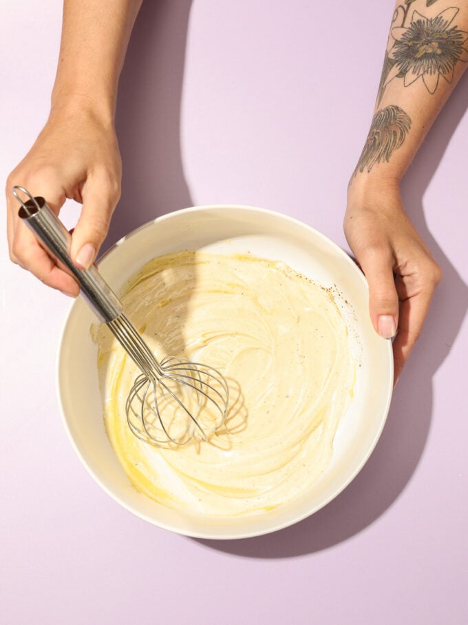 hand whisking coleslaw dressing in white bowl