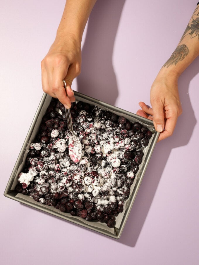 hand stirring blueberries in square pan