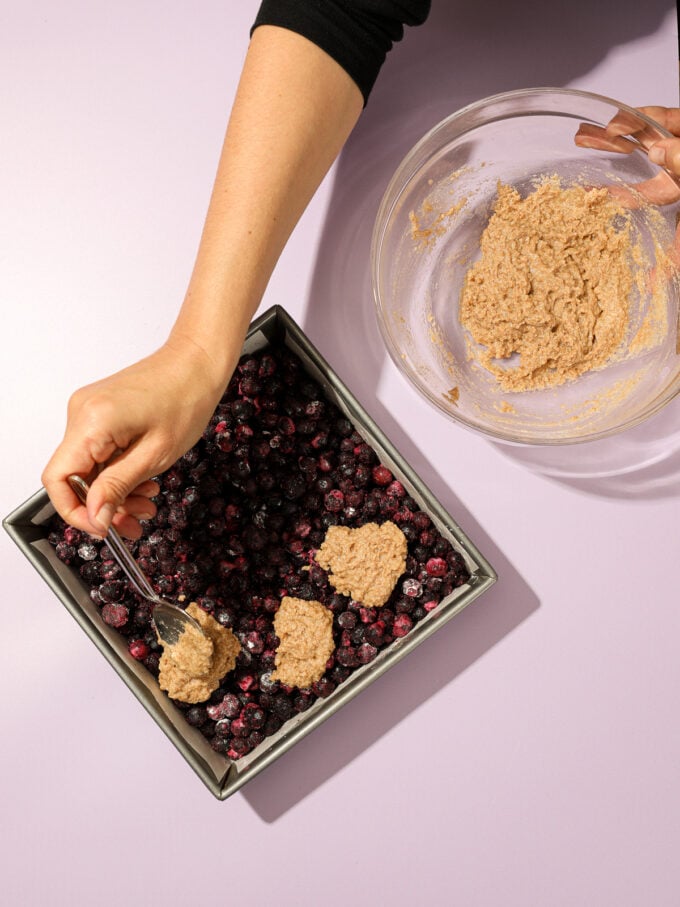 hand adding biscuit topping to blueberry cobbler