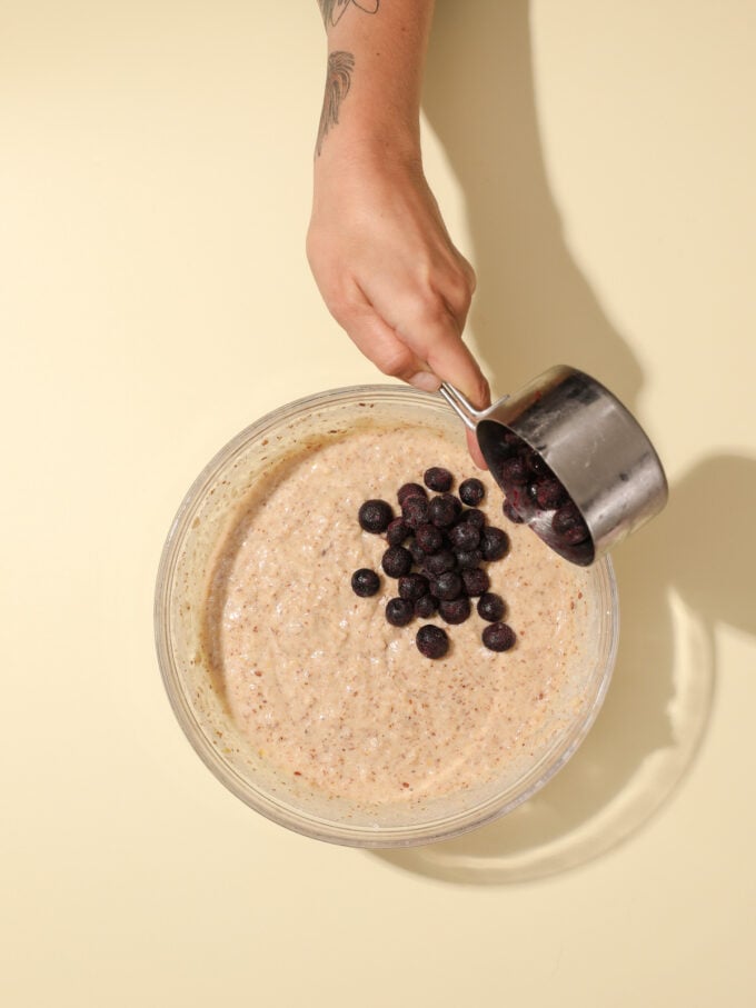 hand adding blueberries to muffin batter