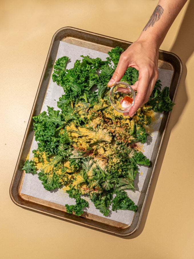 hand sprinkling spices onto kale chips