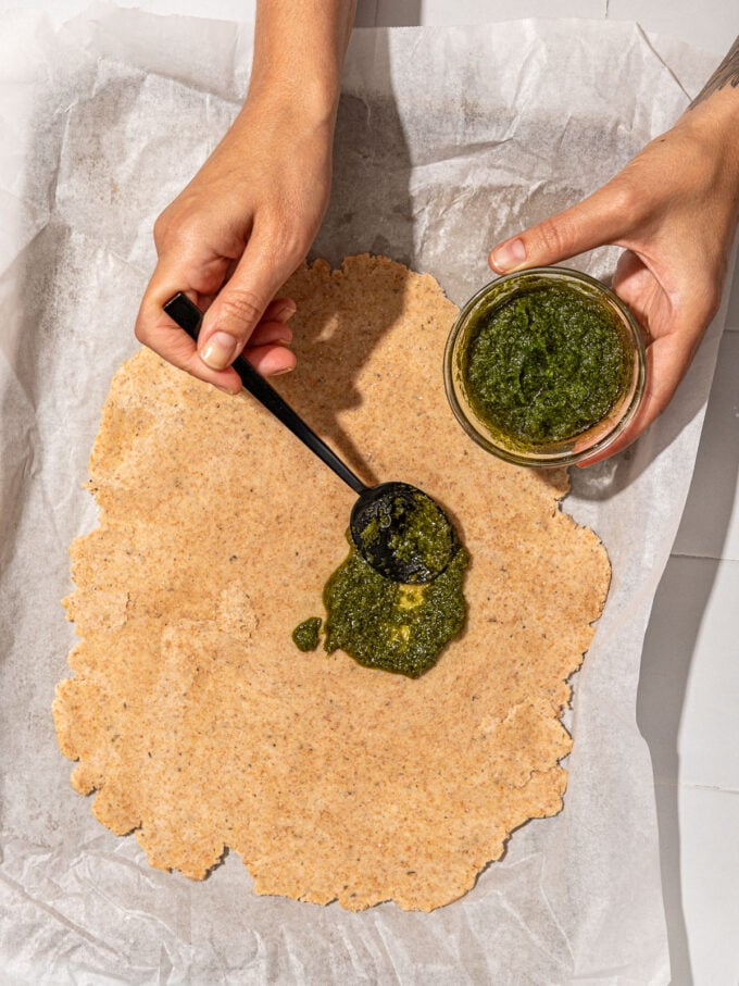 hand spreading pesto on dough