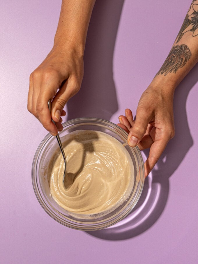 hand stirring tahini and yogurt in bowl