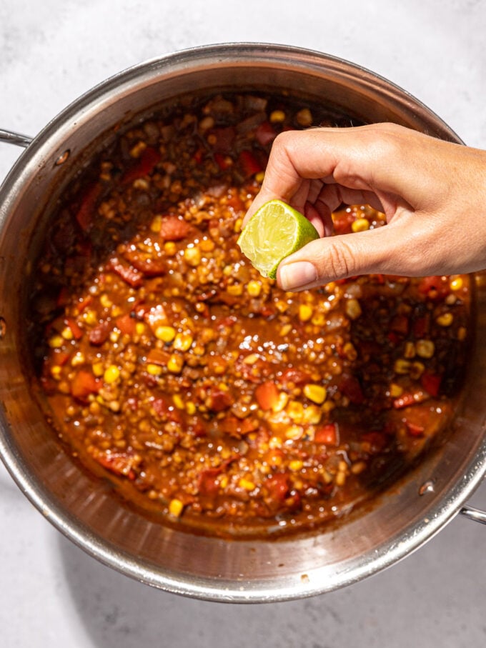 hand squeezing lime into pot of chili