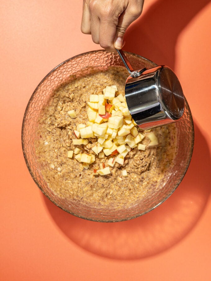 hand pouring apples into muffin batter