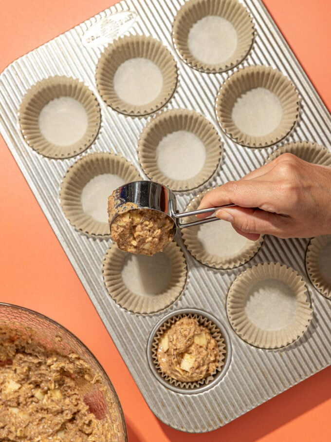 hand portioning apple muffin batter into pan