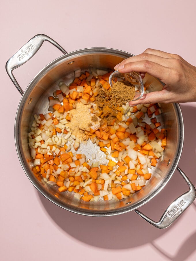 hand pouring cumin into soup pot