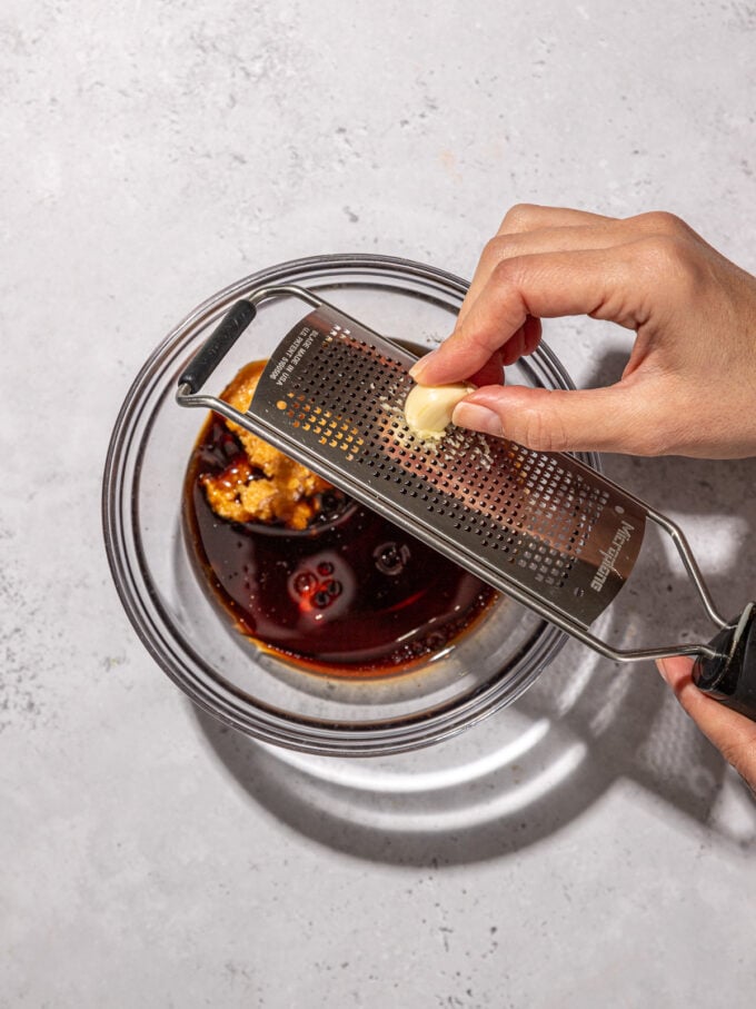 hand grating garlic over bowl