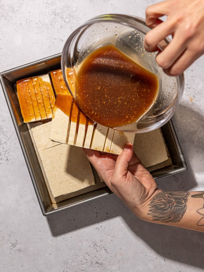 hand pouring marinade over tofu