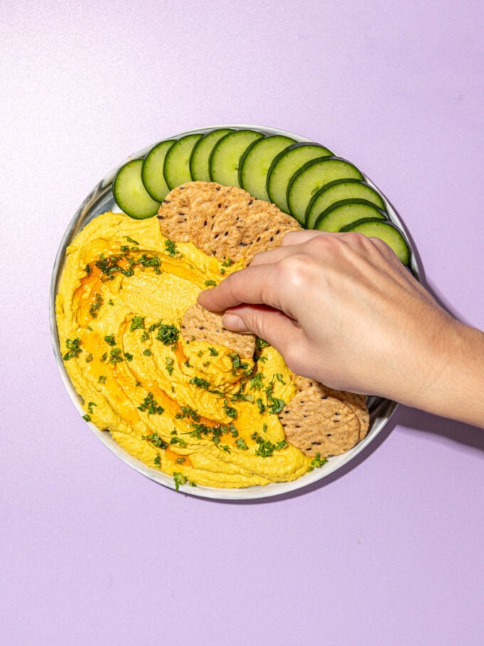 hand scooping red lentil dip with cracker